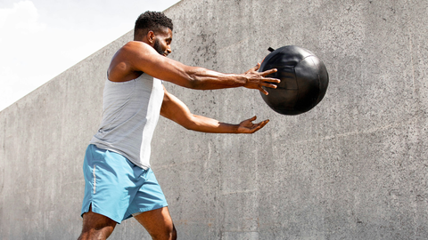 A man working out does wall ball throws with a medicine ball